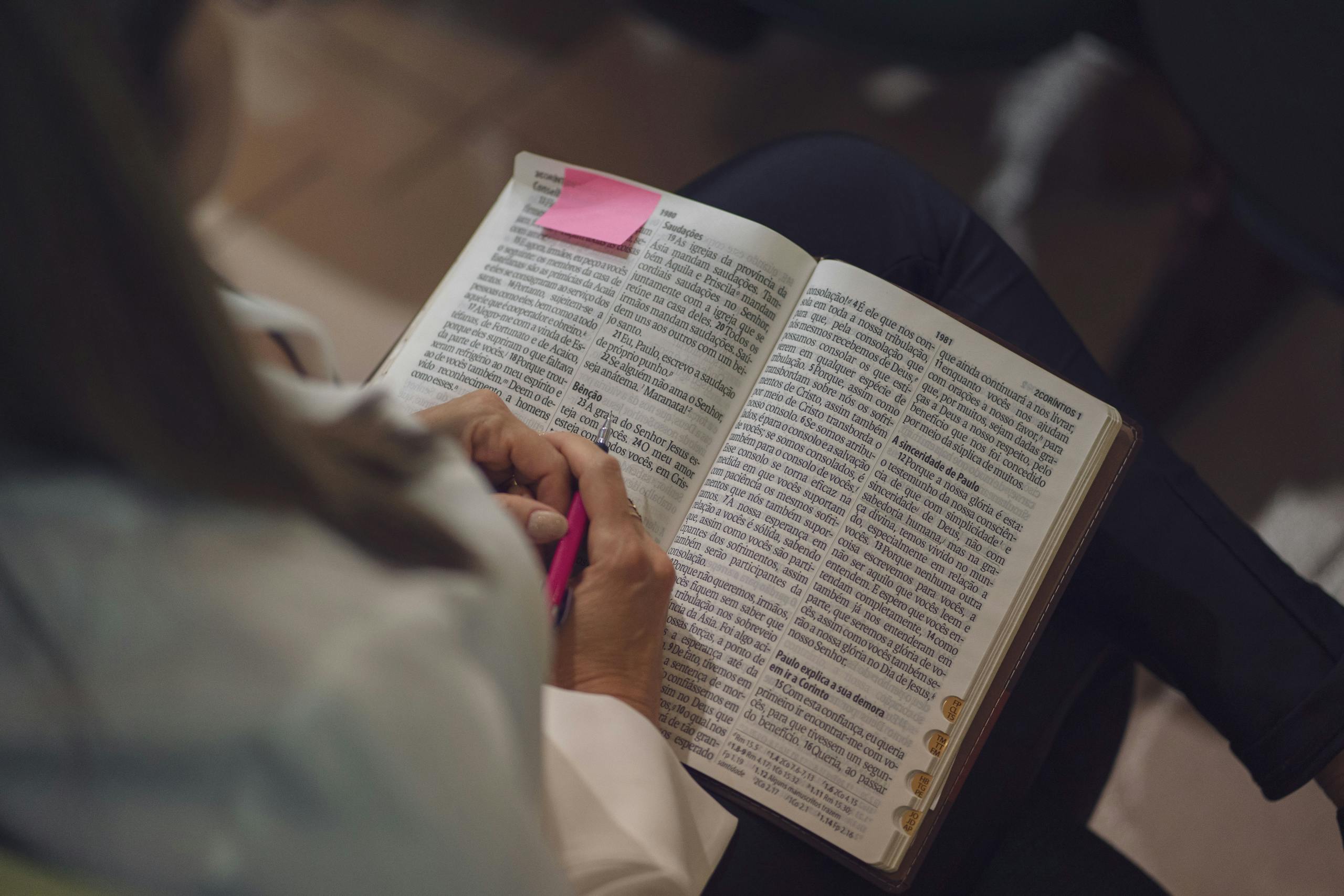 A woman reading a Bible with a pink note, captured indoors showing devotion and study.